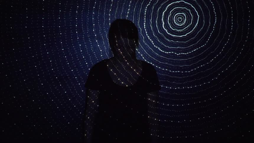 The shadow of a person stands in front of a swirling light on the wall