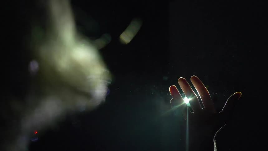 A person holds their hand up in the light of a projector