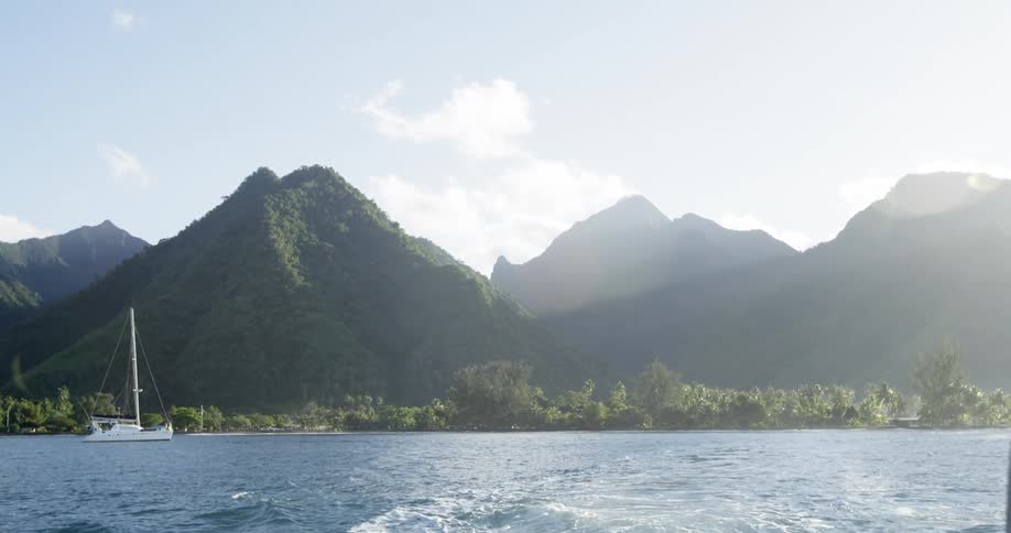 A sailboat sails along the water with hills in the background