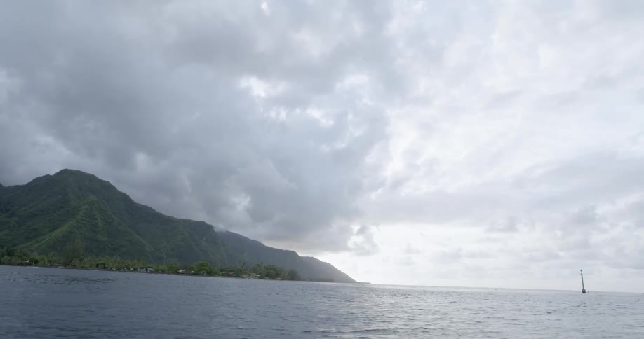 Under a cloudy sky a mountainous shoreline is bordered by the open ocean