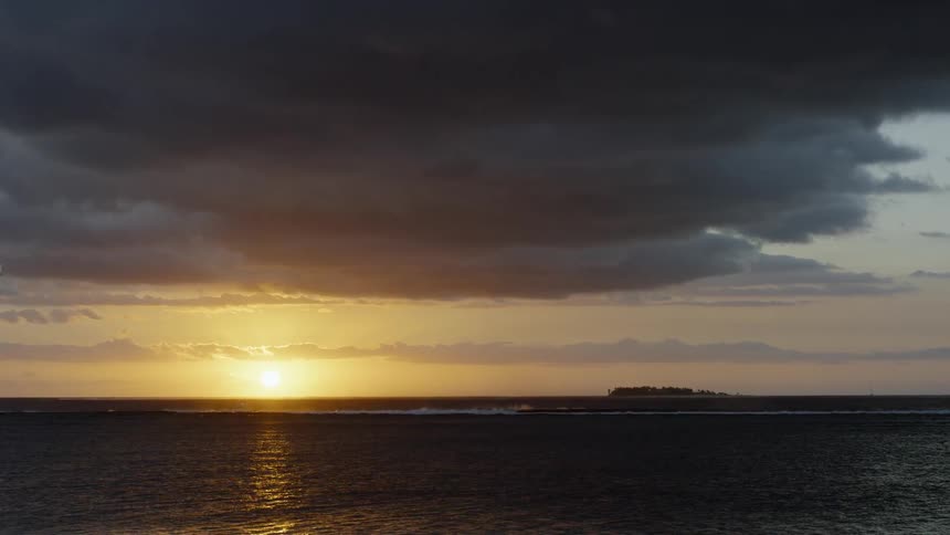 The sun shines low in the sky over the ocean on a cloudy day