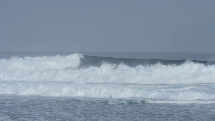 Several sets of ocean waves are seen breaking upon the shoreline