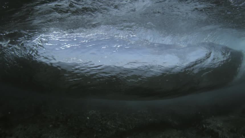 A wave rolling underwater with the sky above