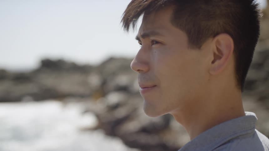 A man stands beside a rocky coast and looks to the ocean water view