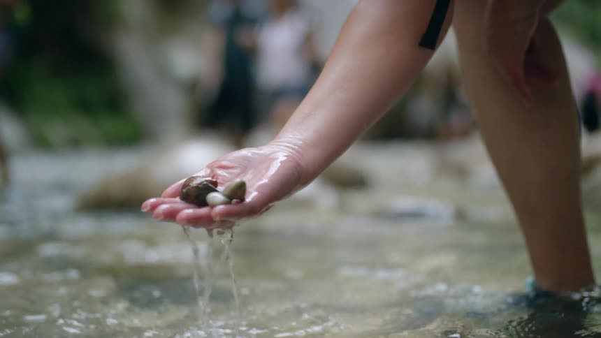 A woman scoops rock up out of a stream