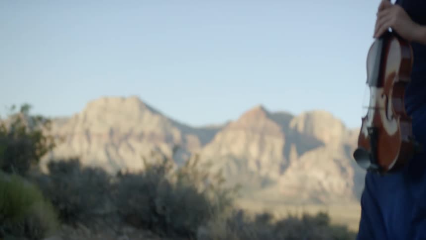 A woman holds a violin while walking along some rocks