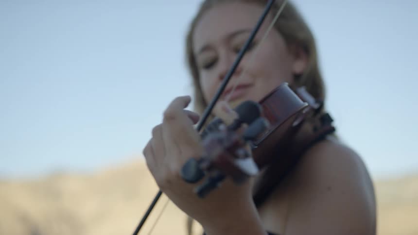 Close up of a blonde haired woman playing violin outdoors