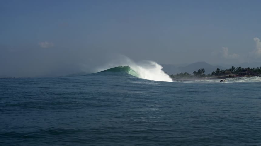 Large waves crash against the shore on a sunny day