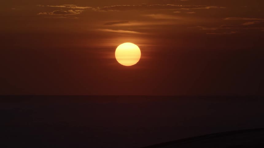 The sun hangs low in the sky just about the horizon while casting a reddish hue