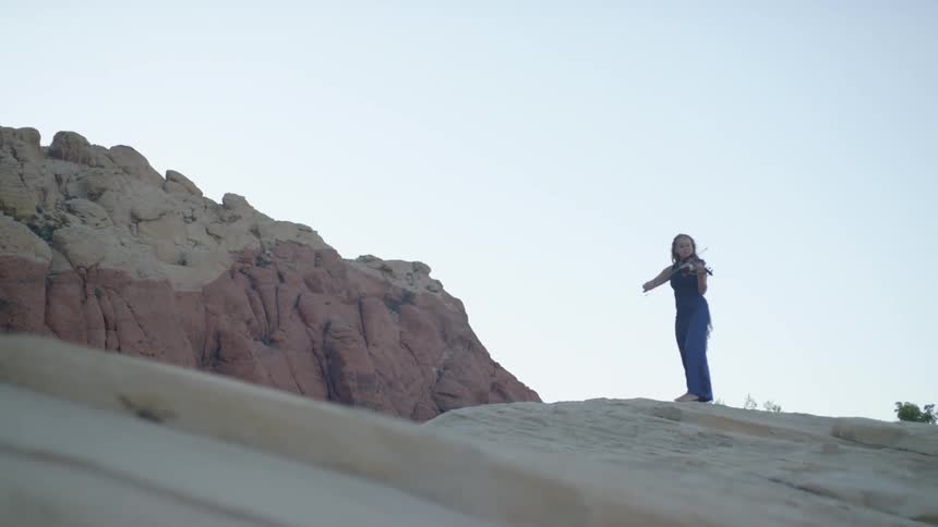 A woman is playing a violin on the rocks ahead