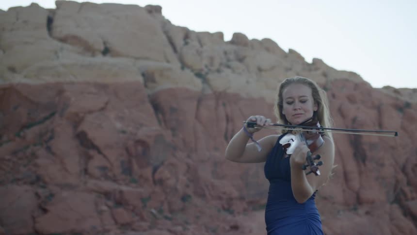 Blonde woman plays on the violin in the canyon
