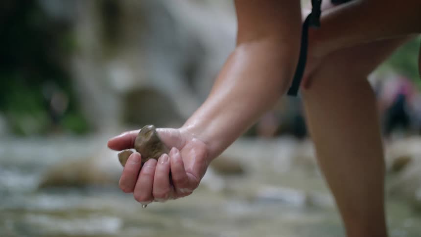 A woman lifts rocks from the stream
