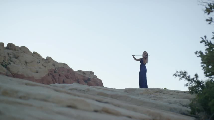 A woman stand on top of a mountain playing the violin