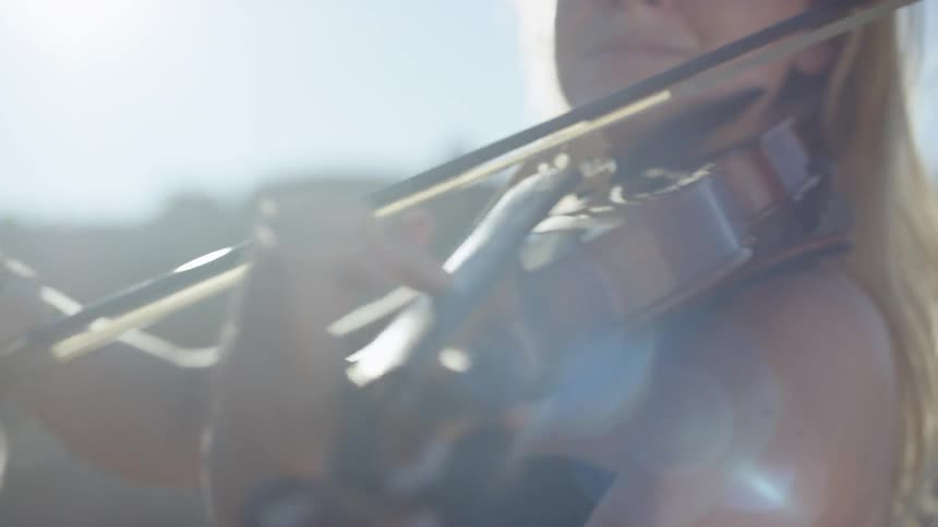 A close view of a woman playing the violin outdoors on a bright and sunny day