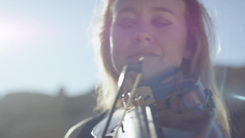A woman outside playing a violin with the sky in the background