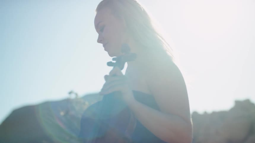Woman in the sunlight carrying a violin walking up a trail in a canyon