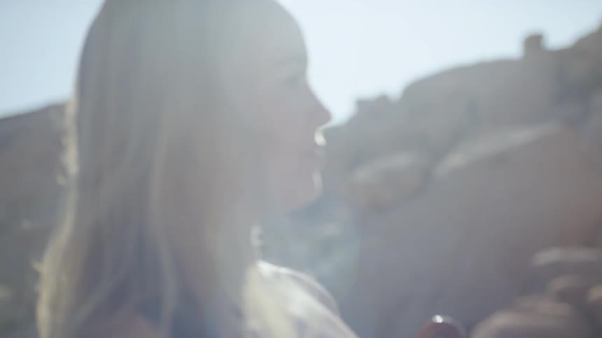 A woman with blonde hair smiles as she look over her shoulder at a large rocky mountain