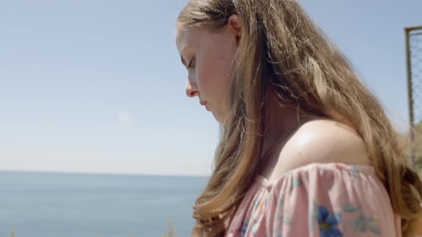 A young girl sketches in a book as she looks out at the water