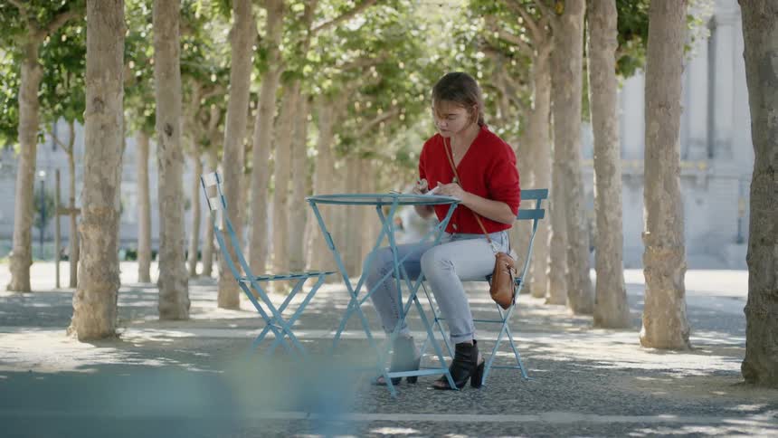A woman sits at an outdoor table flipping through pages of a notebook