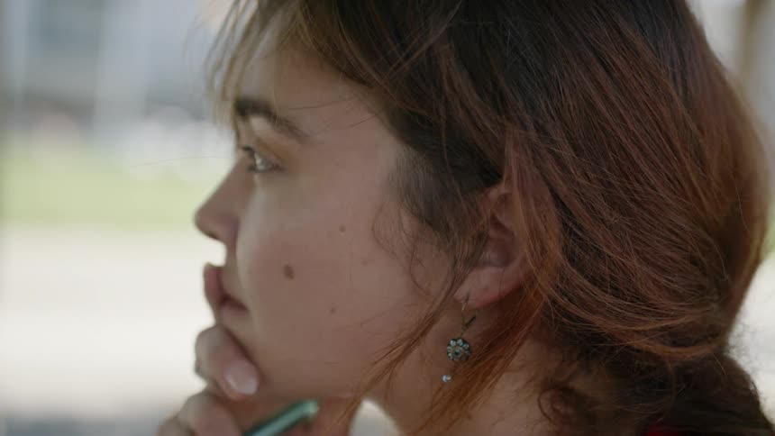 A woman holds a pen and puts her hand to her face as shes thinking