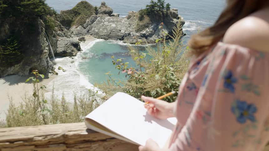 Woman sketching in a notebook along the coast