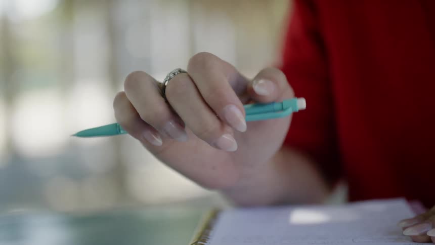 Woman sitting at the table holds a blue pen outdoors