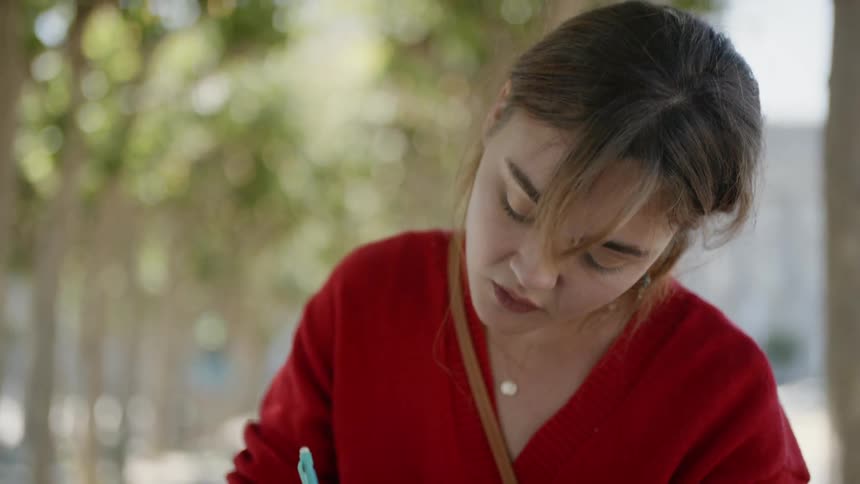 Woman writes in notebook sitting at table outdoors on sunny day