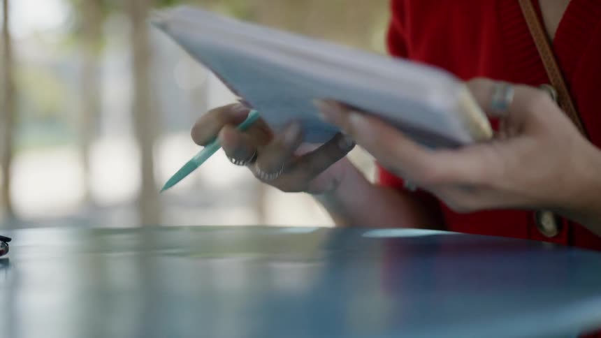 A woman holding a mechanical pencil begins writing on a spiral bound notepad