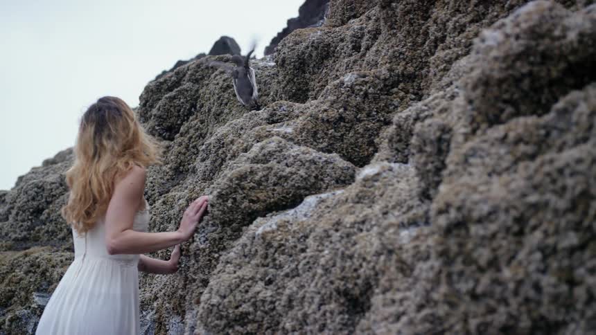 A woman leans against a large rock and sees a bird flapping its wings