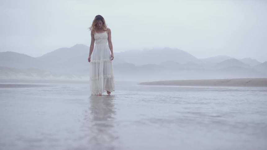A woman is walking in the shallow water by the beach