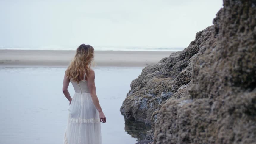 Woman wearing white dress wades into ocean to get closer to seabird
