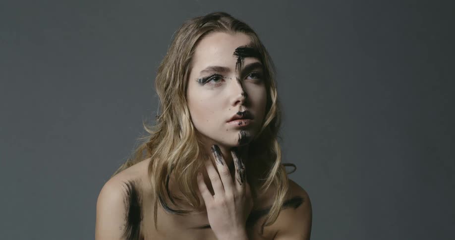 Female model posing in a studio with black paint on her face and body