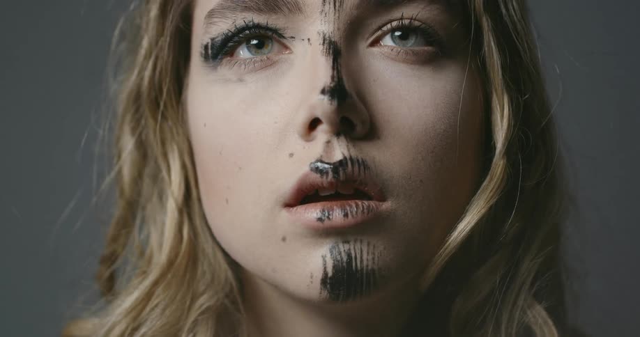 A woman looks around with black paint on her face