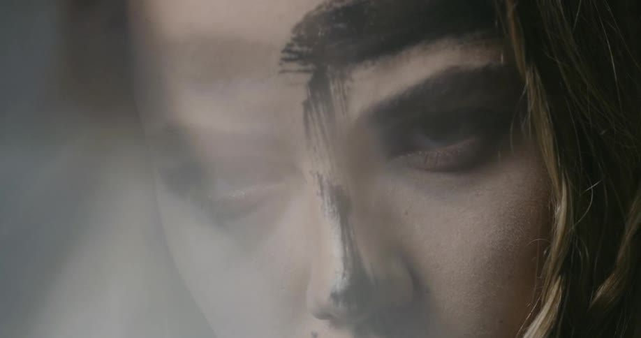 A young woman with black paint on her face stares hauntingly at the camera