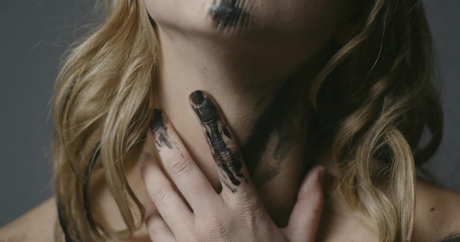 A woman touches her throat with black paint on her hands