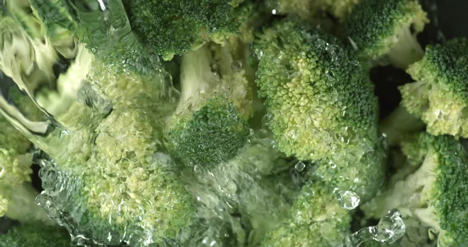 Close up of water pouring on raw cut up broccoli florets