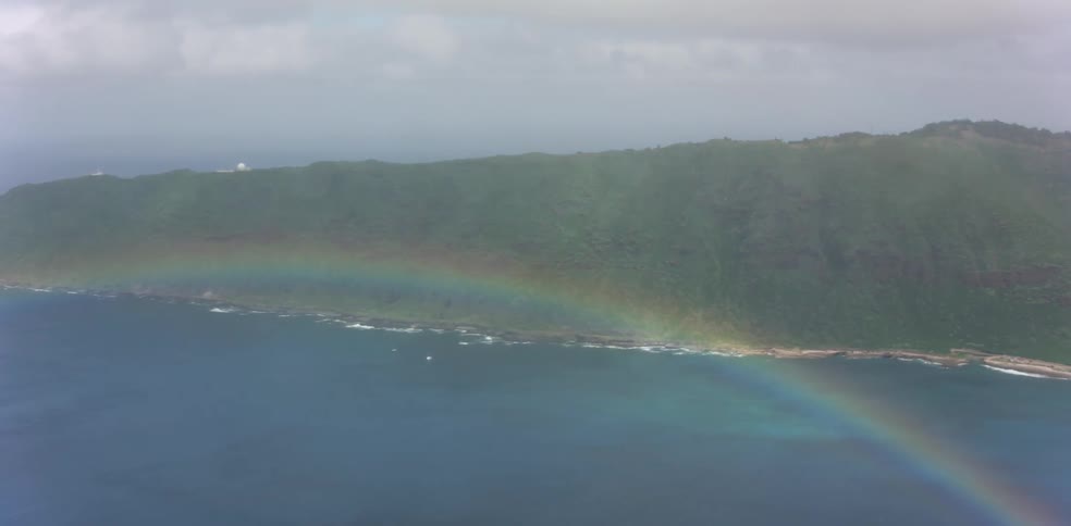 A rainbow over a the ocean near a tree covered peninsula