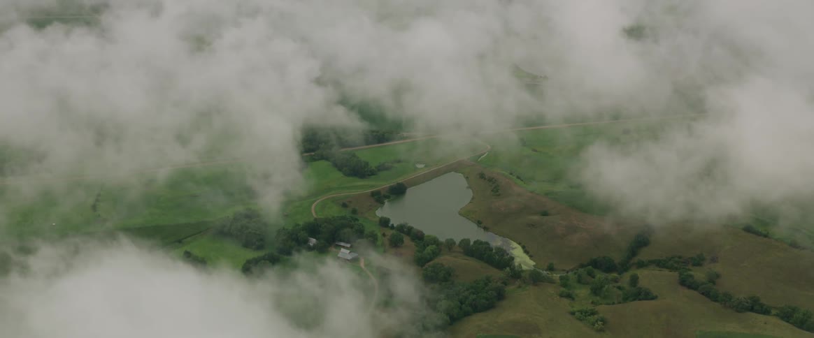 Clouds float over a grassy terrain that surrounds a small lake