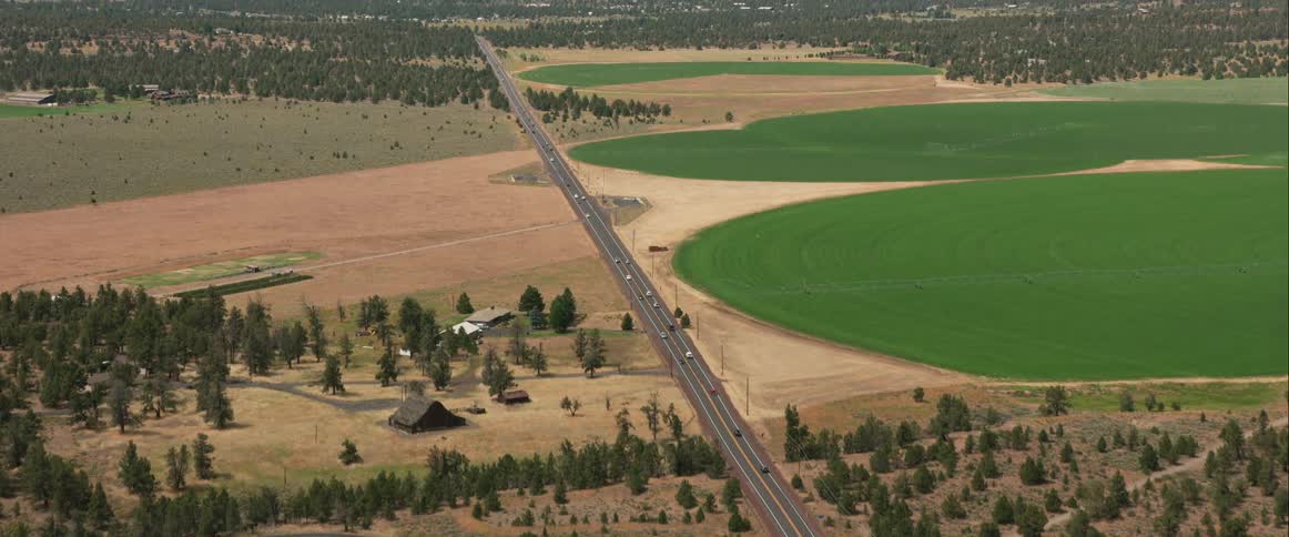 Birds eye view of cars driving down a highway with fields on either side