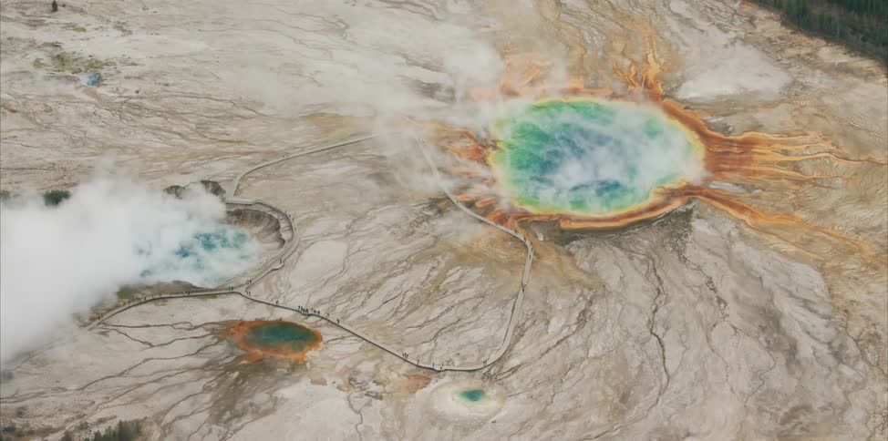 Multihued geothermal pools on rocky terrain bordered by forest