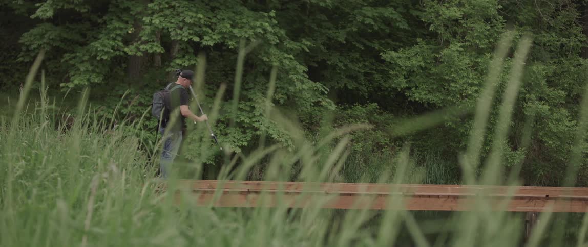 A man stands beside a lake and begins to setup a tripod