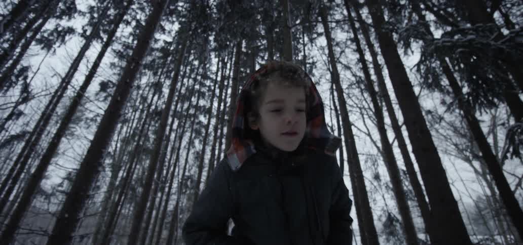 A young boy walks through a snowy forest