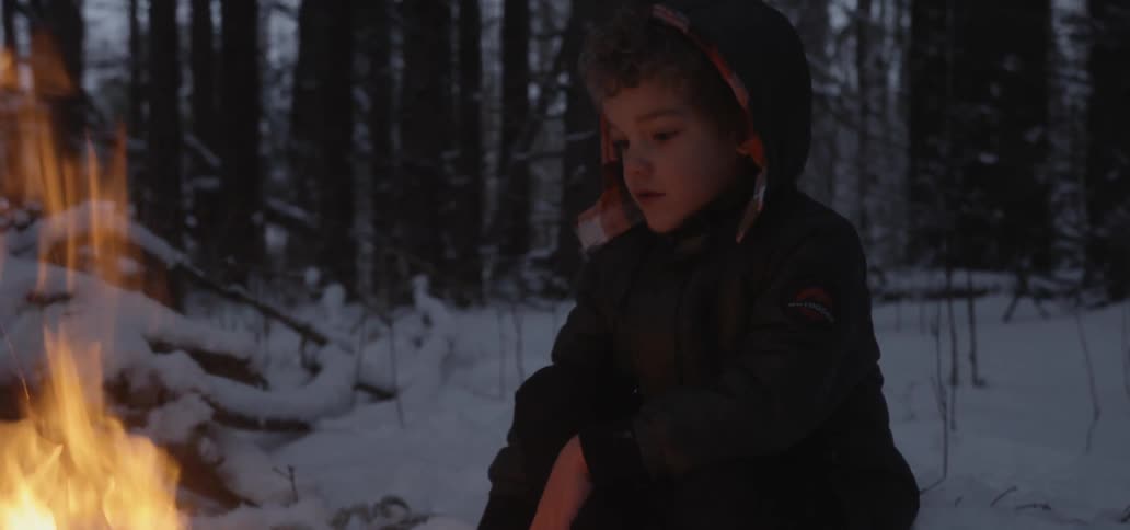 A young boy warms his hands over an open fire