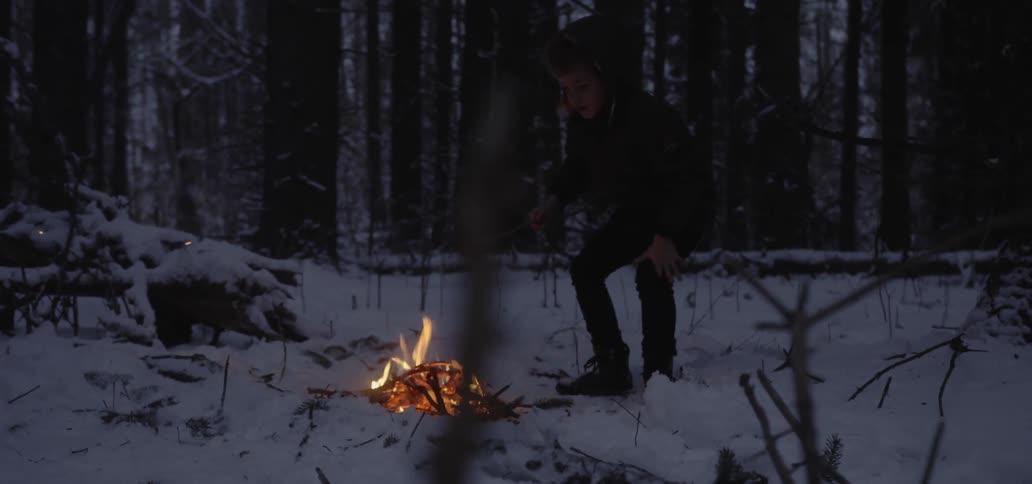 A young boy roasts a marshmallow over a fire in a snowy forest