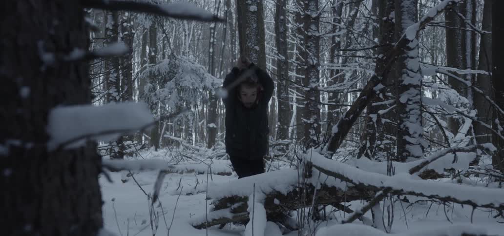A person chops on a log in a snowy forest with an ax