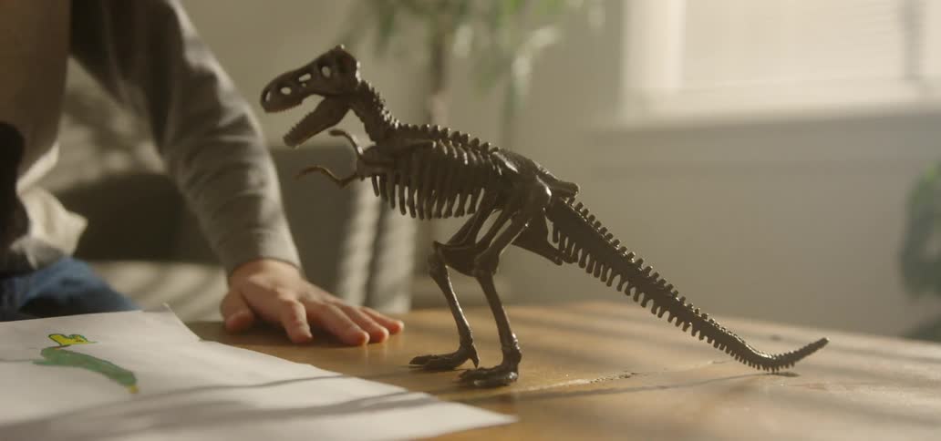 Model dinosaur near a childs drawing as a child approaches the table