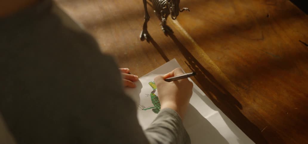 A boy colors in a drawing of a dinosaur based on a toy tyrannosaurus rex
