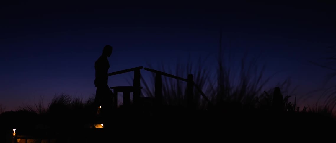 A young woman is silhouetted in the late evening sky as she walks up and over a small bridge