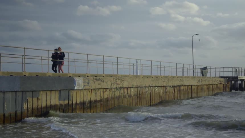 Two people walk down a pier on a cloudy day