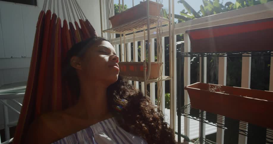 Woman lies in hammock on balcony near potted plants